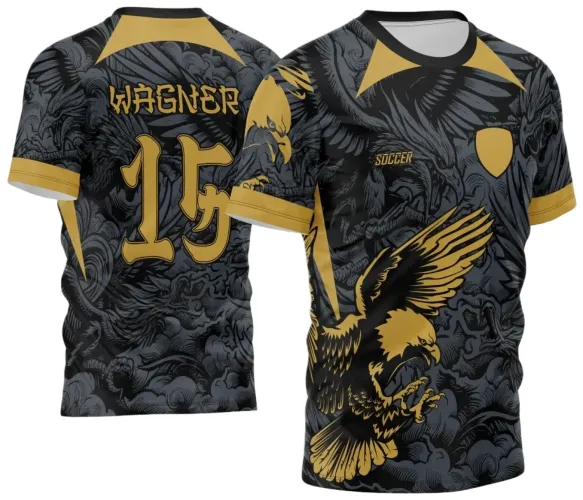 Camisa preta e cinza com estampa de águia dourada em ataque na frente e escudo dourado vazio, texto 'SOCCER'. Nas costas, nome 'WAGNER' e número '15' em dourado com fundo detalhado em nuvens e penas cinzas.