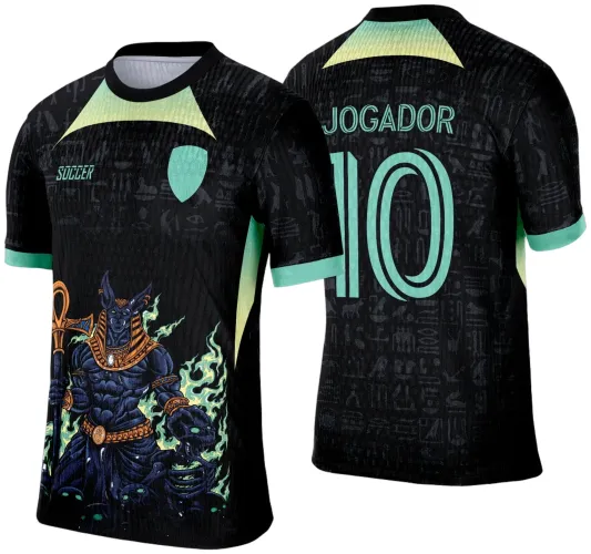 Camisa preta com detalhes verde claro, frente com Anúbis estilizado em preto e dourado segurando cetro, fundo com hieróglifos escuros, costas com número 10 e texto 'JOGADOR' em verde claro sobre hieróglifos.