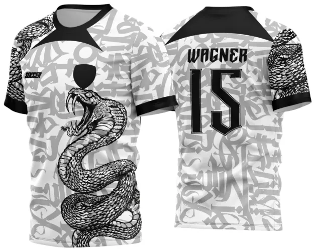 Camisa branca com grafite cinza e cobra preta agressiva na frente, mangas com escamas pretas, gola preta, texto 'SOCCER' e escudo preto frontal. Nas costas, nome WAGNER e número 15 em preto com contorno branco.