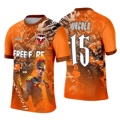 Camisa laranja com personagem de cabelo flamejante e óculos na frente, fundo gráfico em marrom e laranja com textos FREE FIRE, SOCCER e BOOYAH!. Nas costas, número 15 em branco com texto VINCER no topo, sobre fundo com caveira laranja e marrom.