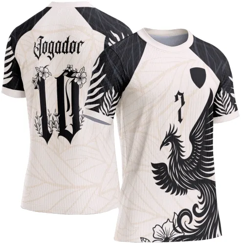 Camisa branca com mangas pretas decoradas com folhas brancas, frente apresenta grande fênix preta, número 7 e escudo preto, costas com texto 'Jogador' e número 10 decorado com flores, fundo bege com padrão folhagem.