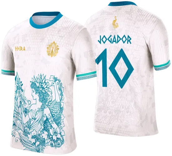Camisa branca com ilustração em azul turquesa de mulher com folhas e pássaro à frente, logo dourado de pavão e texto HERA. Nas costas, nome JOGADOR e número 10 em azul, com pavão dourado no topo, gola e punhos azuis com detalhes gráficos.