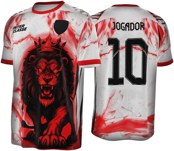 Camisa branca com detalhes em vermelho e preto, frente com leão coroado em pose agressiva, fundo com manchas vermelhas, costas com texto JOGADOR e número 10 em preto, gola e punhos vermelhos e detalhes pretos nos ombros.