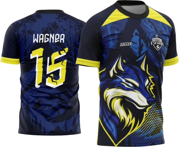 Camisa com fundo azul escuro e detalhes amarelos, apresenta na frente um lobo estilizado em azul e amarelo, com escudo 'SEU ESCUDO' e texto 'SOCCER'. Nas costas, nome 'WAGNER' e número 15 amarelo com contornos brancos sobre padrão de montanhas.