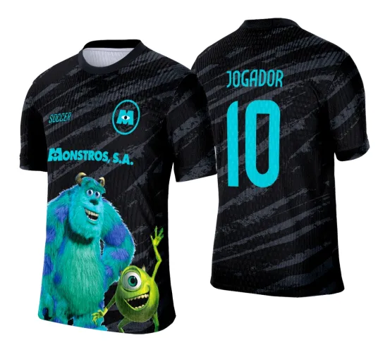 Camisa preta com fundo texturizado em linhas diagonais; na frente, Sulley e Mike dos Monstros S.A. em cores vibrantes com textos 'SOCCER' e 'MONSTROS, S.A.' em azul turquesa; costas exibem nome JOGADOR e número 10 também em azul.