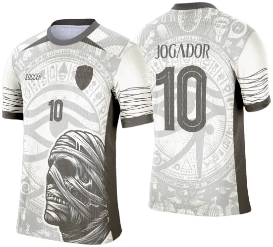 Camisa branca com laterais cinza escuro, frente com figura detalhada de múmia na parte inferior, número 10 e escudo preto, costas com nome JOGADOR e número 10 grandes em cinza sobre fundo de símbolos egípcios.