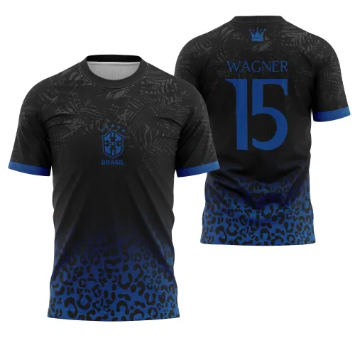 Camisa com frente preta decorada por folhas cinza escuro, degradê azul e estampa de onça, escudo CBF e BRASIL em azul. Costas exibem número 15 e nome WAGNER em azul, com coroa azul no topo, tudo sobre fundo preto com estampa de folhas e onça em degradê azul.