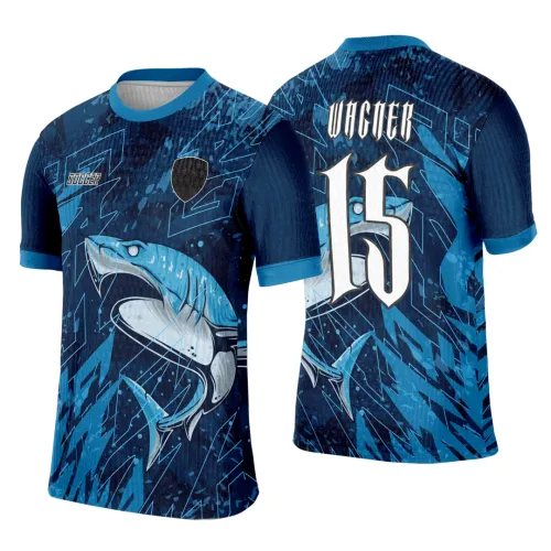 Camisa azul escura com tubarão azul estilizado na frente, gola e punhos em azul celeste, escudo preto. Nas costas nome VACNER acima do número 15 branco grande e estilizado, tubarão visível ao fundo em degradê azul.