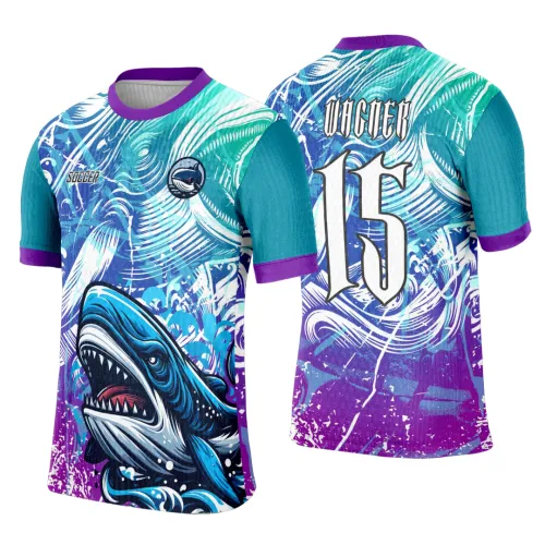 Camisa com tubarão azul em destaque na frente, fundo roxo e azul com ondas e detalhes brancos, mangas azul turquesa com punhos roxos e gola roxa; costas com número 15 branco e nome VAGNER em fonte estilizada.